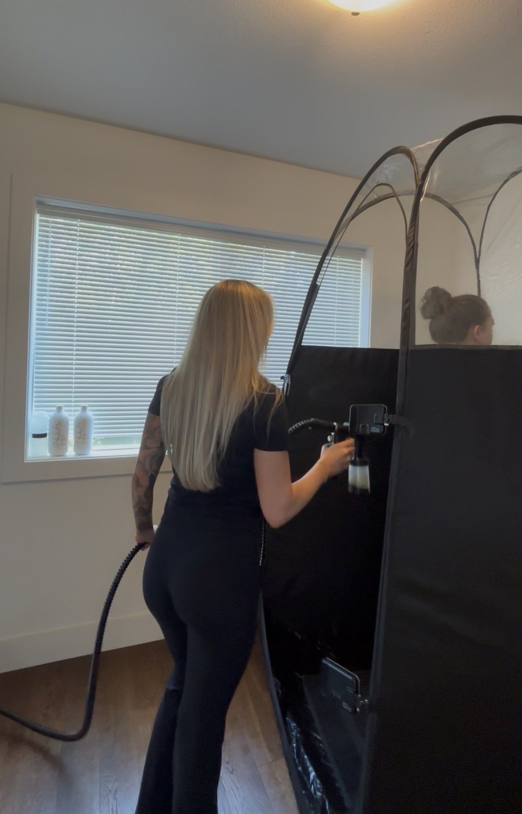 Savanna spraying a client inside the pop-up tent at a mobile appointment