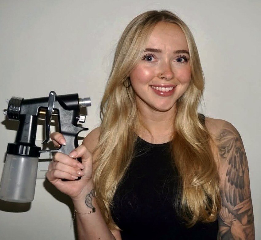 Savanna, founder of Bronzed Behaviour, holding her spray tan airbrush
